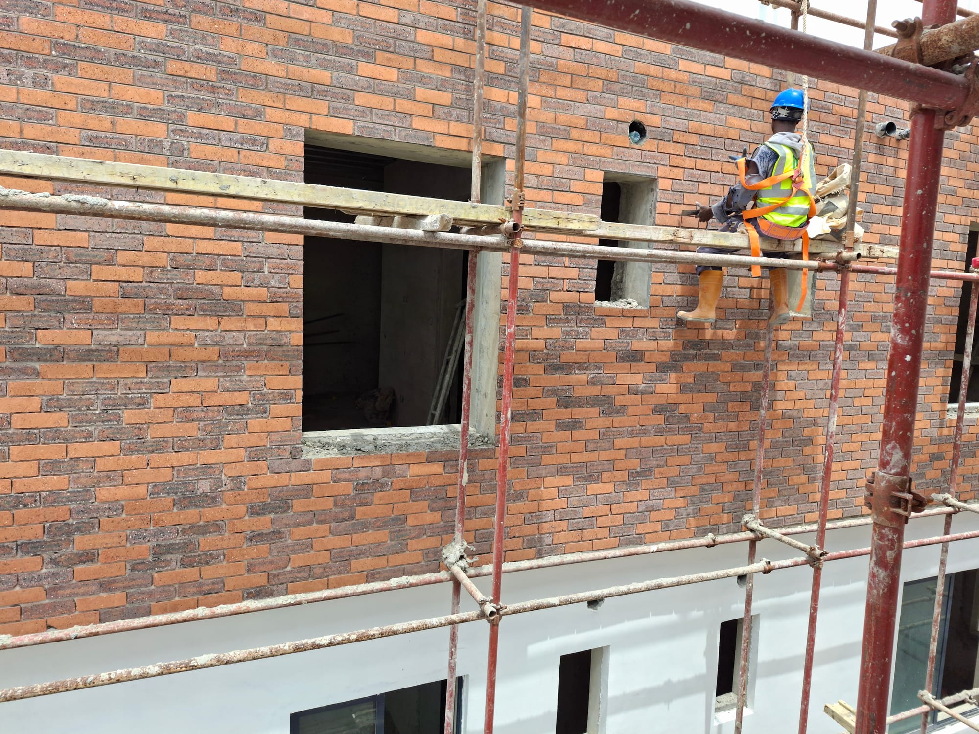 Soapworth operative in full PPE and safety harness installing brick facade from scaffolding